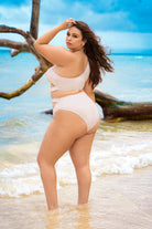 Plus size model wearing CT Lingerie cora shimmery plus size swimsuit standing on beach with ocean background